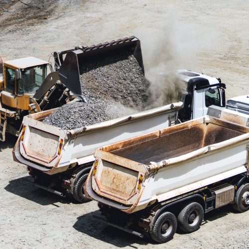 wheel loader bulldozer loading two dumper trucks in sandpit at highway construction site